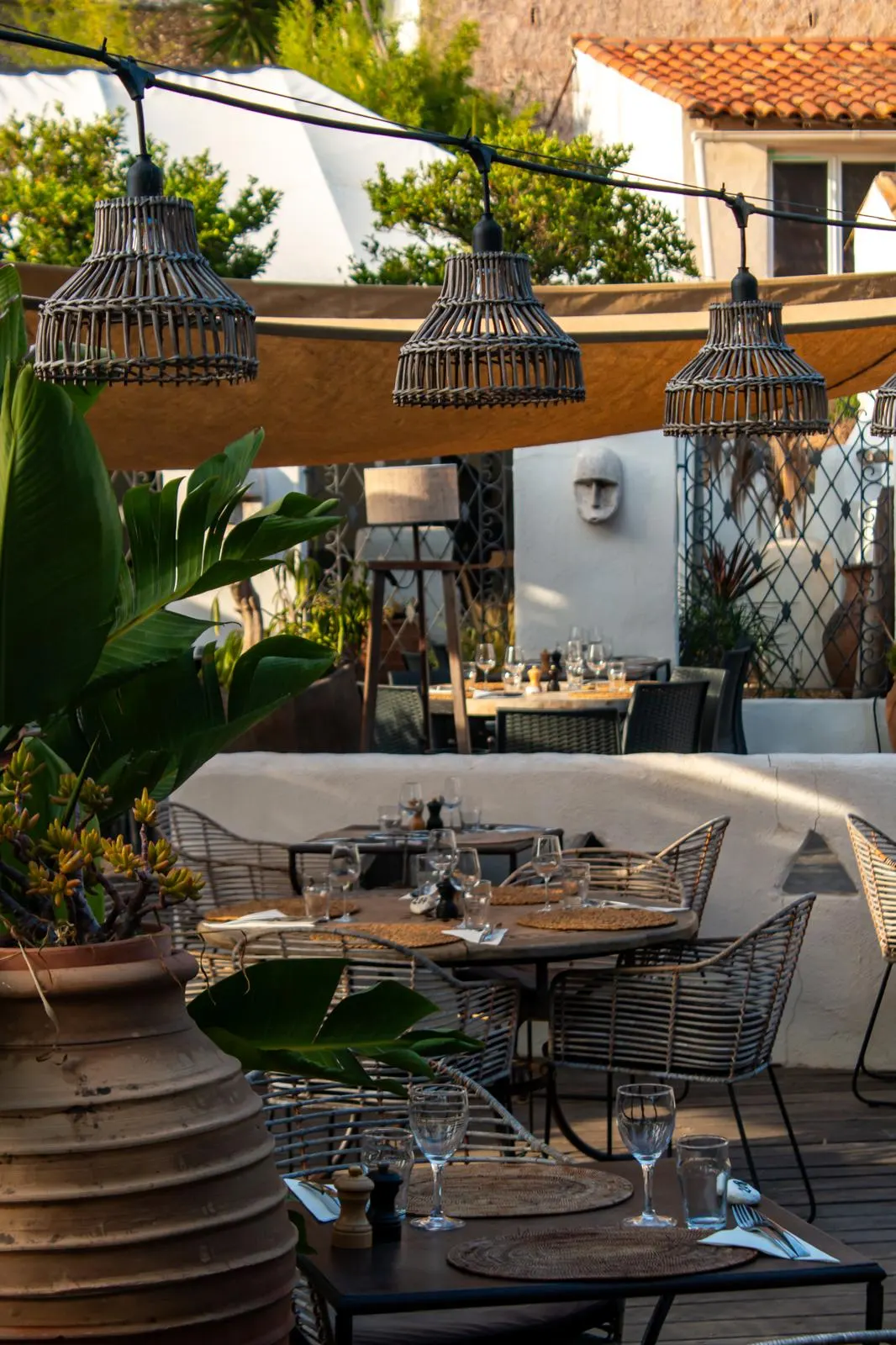Terrasse de Nomade avec suspensions en osier, voilage et tables dressées parmi les plantes
